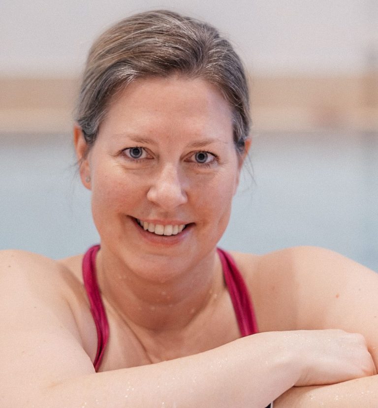 Eine lächelnde Frau, die im Wasser steht und einen pinken Badeanzug trägt.