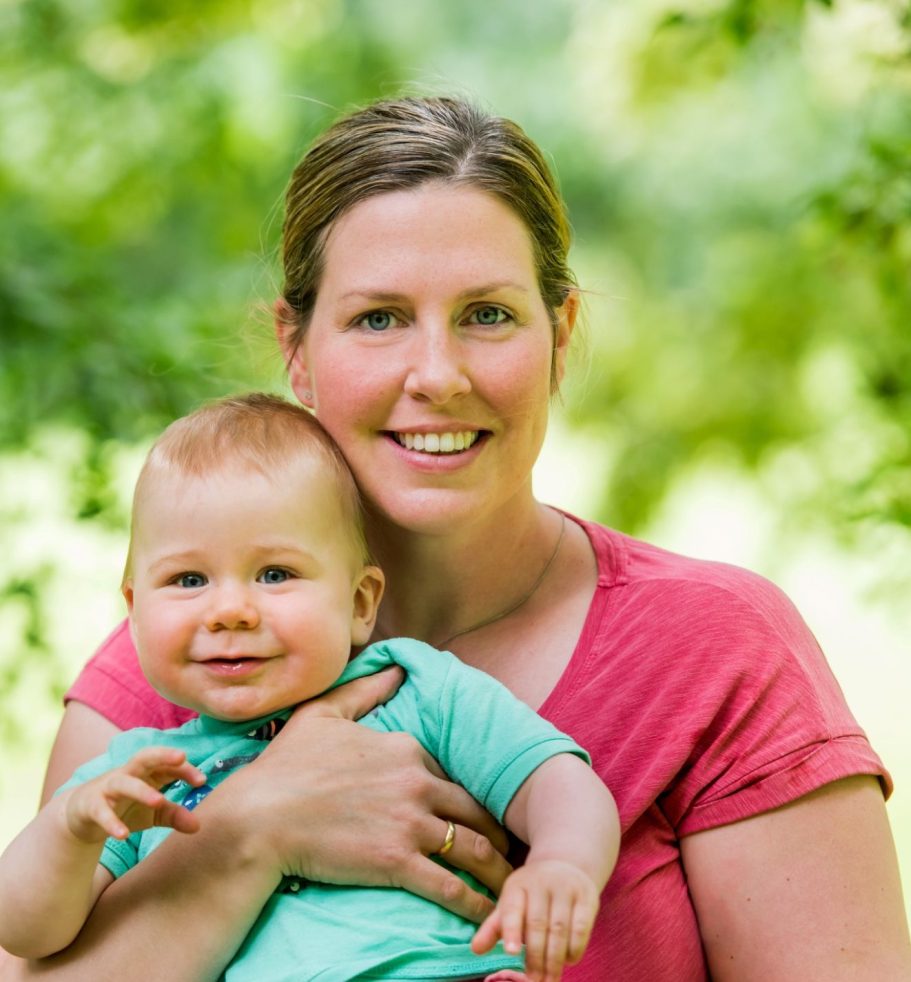 Eine lächelnde Frau hält ein lächelndes Baby in einer grünen Umgebung.