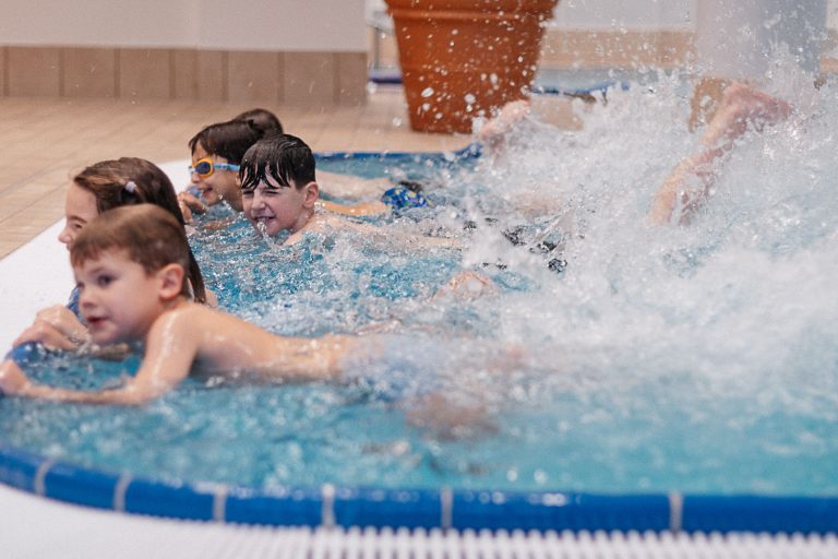 Bewegungsfreude bei SwimFox Fünf Kinder im Wasser, einer spritzt Wasser, alle haben Spaß im Schwimmbad.