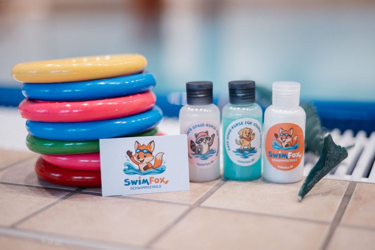 SwimFox Zubehör Bunte Schwimmreifen, Pflegeprodukte und ein Schild mit einem Fuchs-Logo.